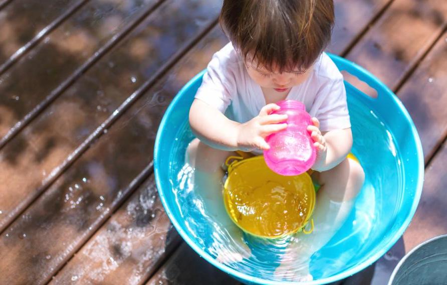 Toddler in a kiddie pool drinking out of a pink sippy cup