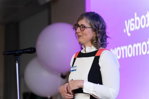 Woman with glasses talking at microphone.