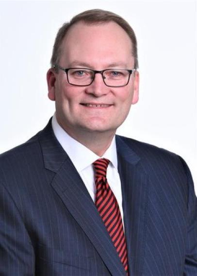 White man with glasses in a navy suit with red striped tie